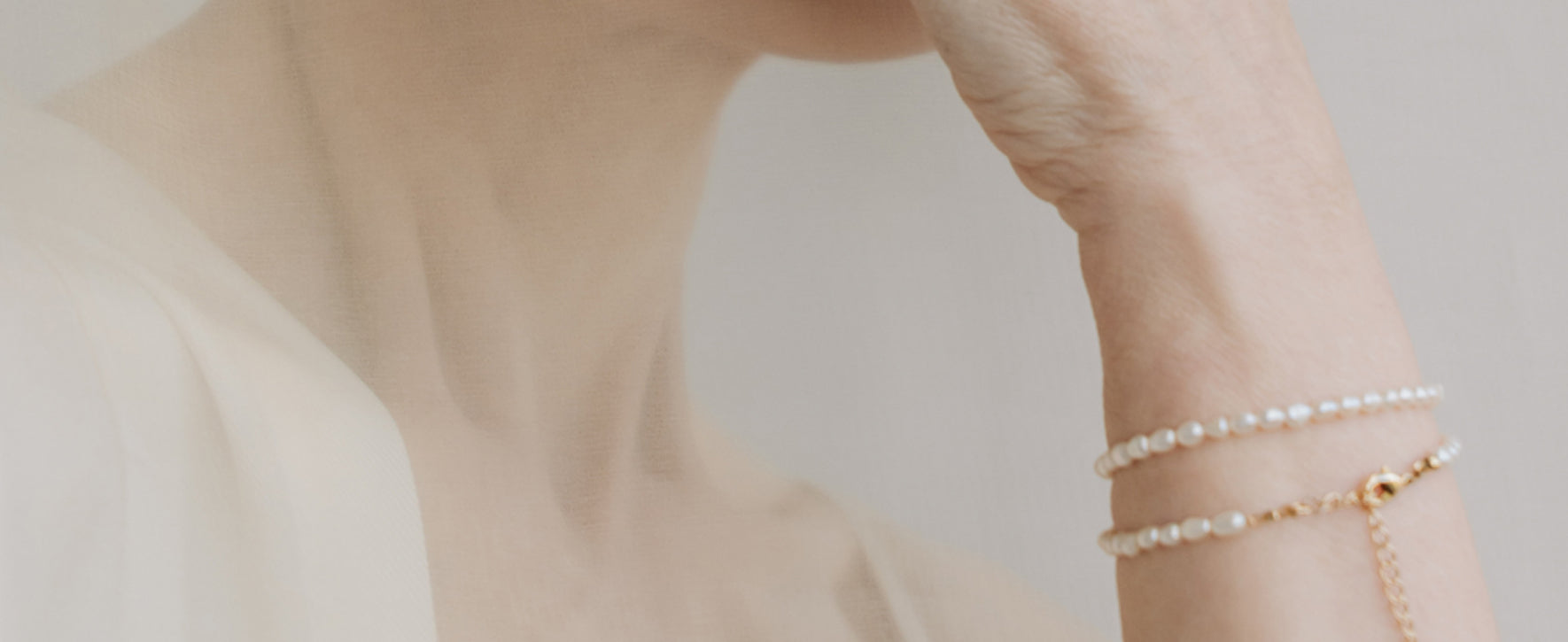 Close-up of a person wearing multiple pearl bracelets on a neutral background
