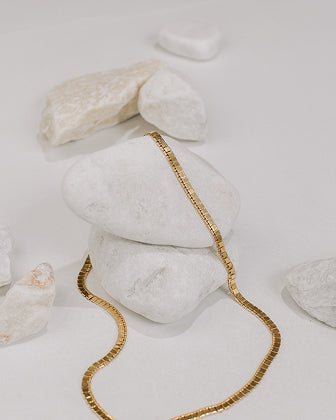 Gold chain on a white stone surface with a minimal background