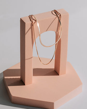 Gold necklace on a pink jewelry stand against a light gray background
