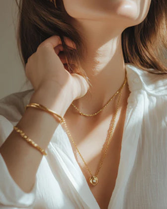 Person wearing a gold necklace and bracelet against a neutral background
